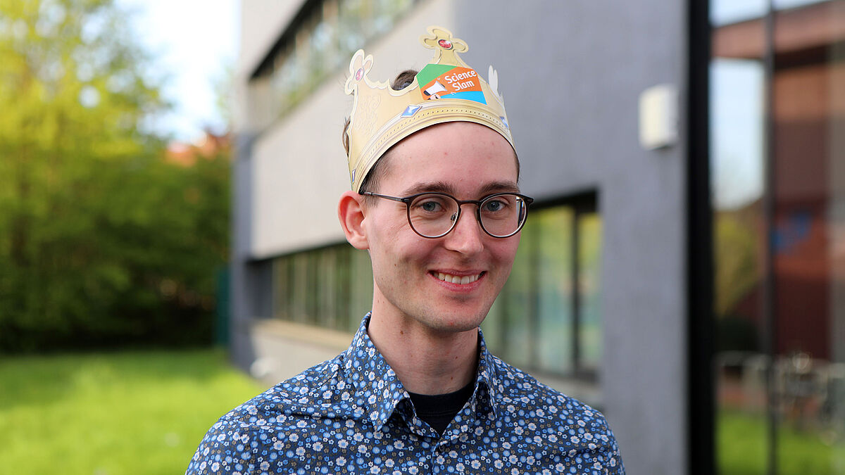 König Der Science Slam-Siger ist mit einer Pappkrone auf dem Kopf im Porträt zu sehen.