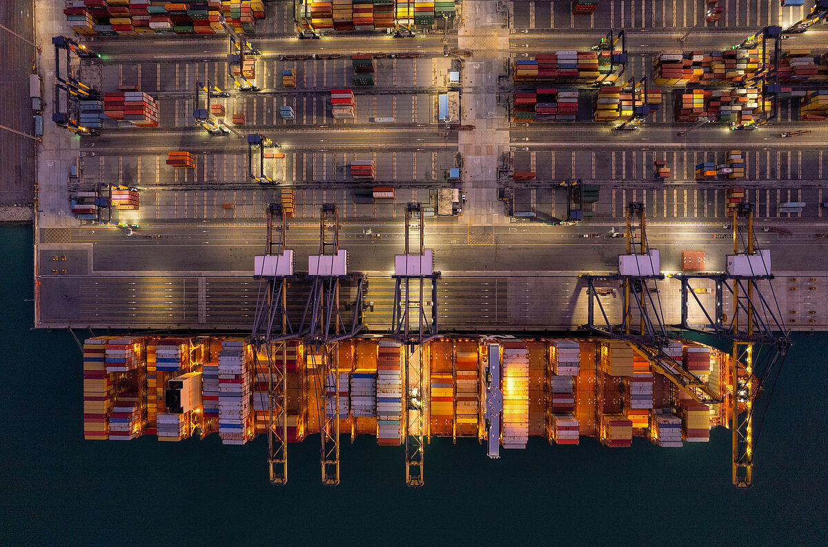 Introduction_Image_Symbolbild_DLM_Master_SL_2023 Introduction_Image Studiengang DLM Master Auf einem Seehafengelände werden Container auf ein Schiff umgeschlagen. Draufsicht.