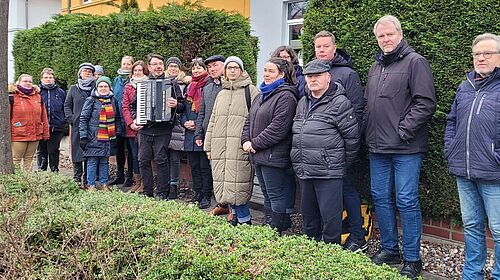 Auf dem Gehweg zwischen geschnittenen Hecken steht eine Gruppe von Personen aufgereiht und schaut in die Kamera.