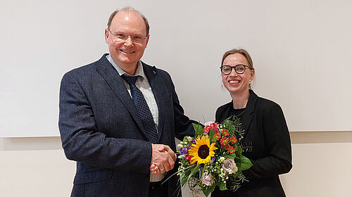 Der Senatsvorsitzende schüttelt Frau Dr. Bernier die Hand und überreicht einen Blumenstrauß.