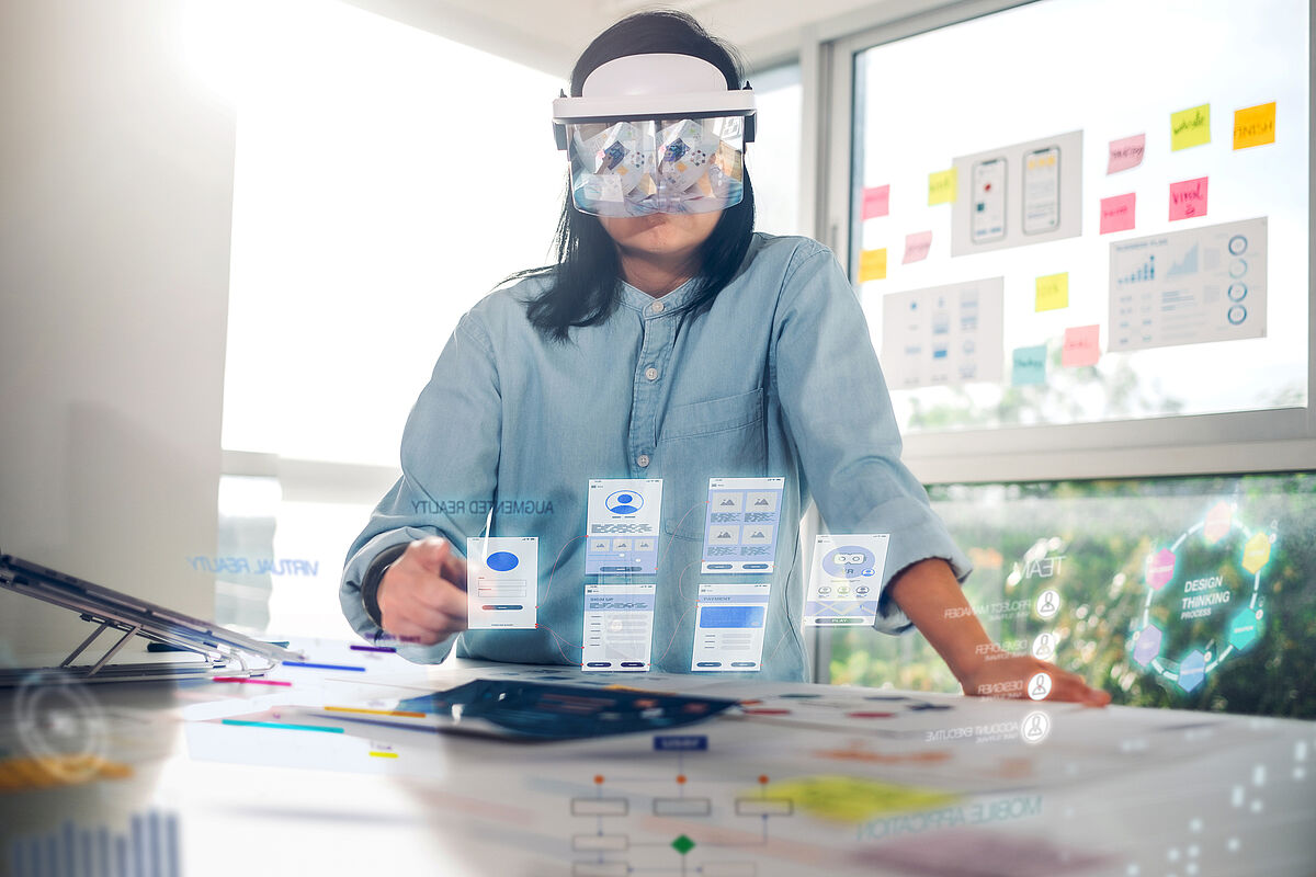 Introduction_Image_Symbolbild_WI_Master_SL_2023 Introduction_Image Studiengang Wirtschaftsinformatik Master Eine Frau mit AR Brille sieht vor sich virtuelle Tabs vor einem Tisch