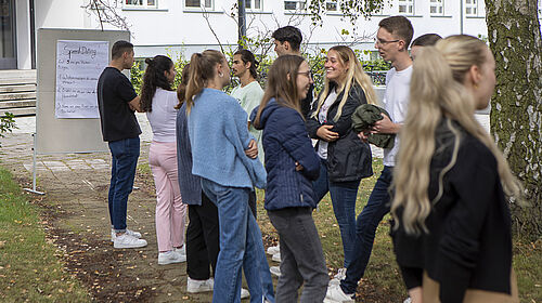 Zwei Reihen Studierende stehen sich gegenüber und sind ins Gespräch vertieft. Im Bildhintergrund steht ein Whiteboard mit der Aufschrift "Speeddating"