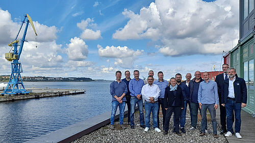 Die Gruppe steht auf der Dachterasse vor dem Konferenzraum des TZF. Über ihr ist ein wunderschöner Himmel mit Wolken zu sehen.